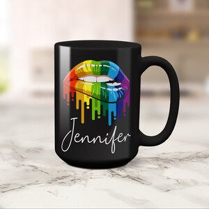 May include: Black coffee mug with a rainbow dripping lips design and the name Jennifer in white script.