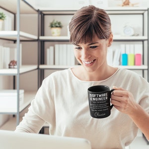 K&ouml;nnte beinhalten: Schwarze Kaffeetasse mit wei&szlig;em Text, der "Software Engineer" lautet und eine Definition des Begriffs enth&auml;lt. Die Tasse tr&auml;gt au&szlig;erdem den Namen "Olivia", der darauf gedruckt ist.