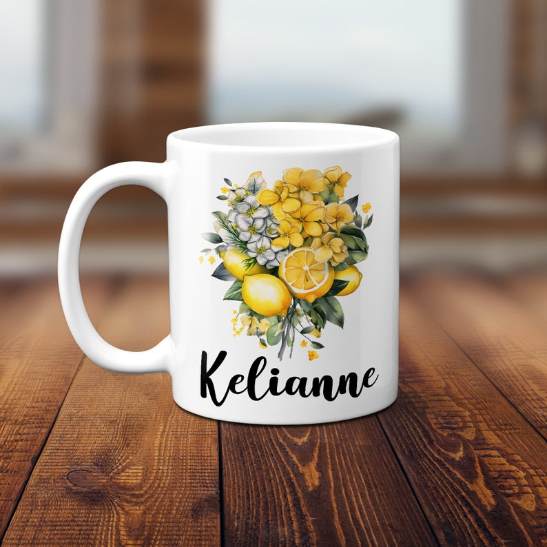 May include: White ceramic mug featuring a vibrant floral design with lemons, yellow flowers, and green leaves. The name "Kelianne" is written in black script below the design. The mug has a curved handle.