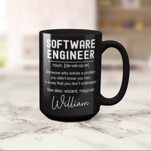 K&ouml;nnte beinhalten: Schwarze Kaffeetasse mit wei&szlig;em Text, der lautet: "SOFTWARE ENGINEER noun. [de-vel-op-er] Someone who solves a problem you didn't know you had, in a way that you don't understand See also: wizard, magician William"