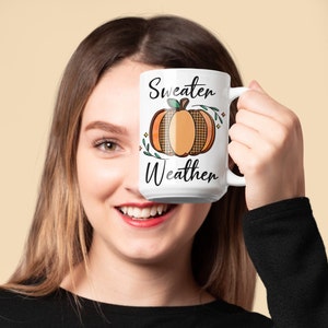 May include: White ceramic mug with a black and orange pumpkin design and the text "Sweater Weather".