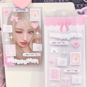 May include: A clear plastic sheet with pink and white stickers. The stickers include hearts, bows, stars, and stamps with a teddy bear and a girl's face. The text on the stickers is in a foreign language.