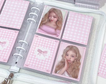 May include: A clear, glittery binder with a zipper closure, filled with pink and white checkered card inserts. The inserts hold photos of a woman in a pink top. The binder is open, revealing the contents.