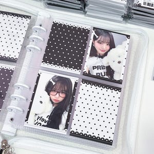 Può includere: Un album fotografico trasparente con cerniera con più tasche contenenti foto e inserti decorativi a pois bianchi e neri. Le foto mostrano giovani donne che tengono in mano animali di peluche. L'album è aperto, mostrando diverse pagine.