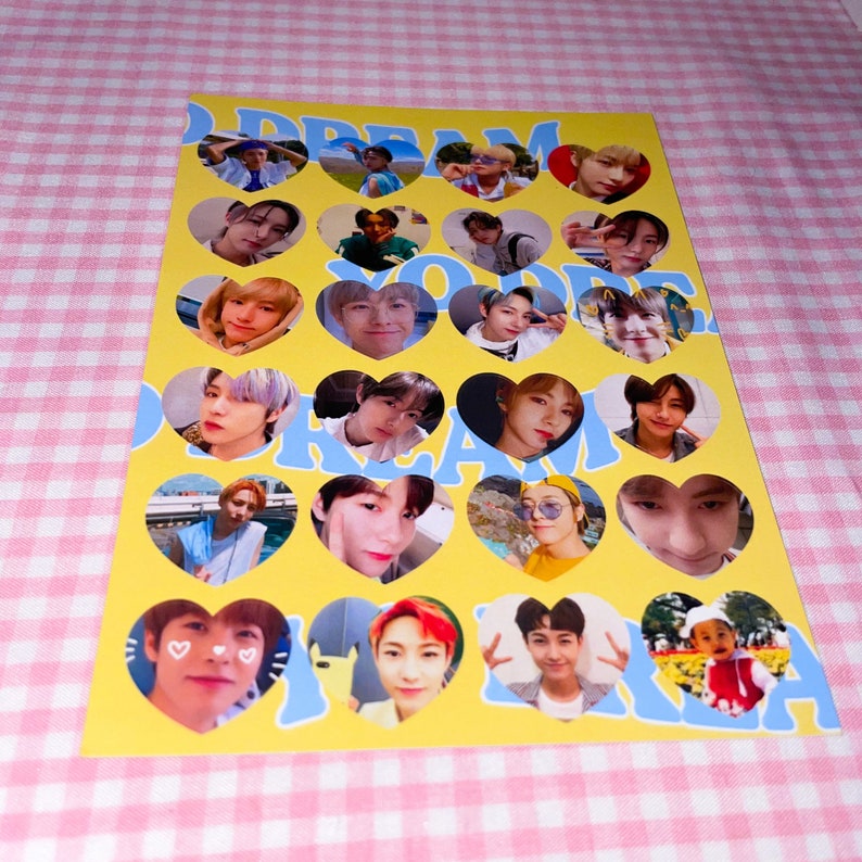 Op de afbeelding: Een gele en blauwe stickervel met hartvormige frames met foto's van een jongensband. De tekst "DREAM YOU'RE DREAM" staat op het vel gedrukt.