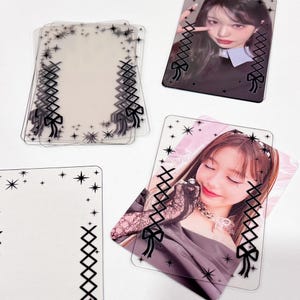 Puede incluir: Un conjunto de porta tarjetas de fotos de plástico transparente con un diseño de encaje negro y lazo. Los porta tarjetas tienen un patrón de estrellas alrededor de los bordes.