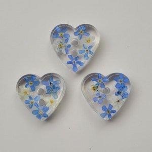 May include: Three heart-shaped buttons with blue forget-me-not flowers pressed into clear resin.