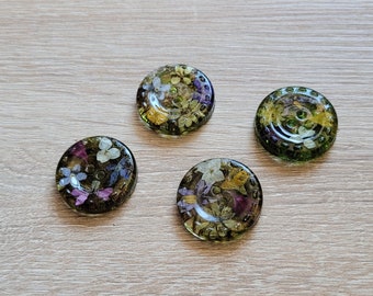May include: Four green resin buttons with embedded pressed flowers. The buttons have a raised edge and a flat surface. The flowers are a mix of white, yellow, and purple.
