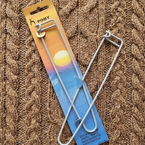 May include: Two silver-colored stitch holders with a blue and yellow card. The card has the word "PONY" and a logo of a horse. The stitch holders are designed for knitting and crochet projects.