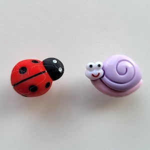 May include: A red ladybug with black spots and a purple snail with a white face. These are small plastic figurines.