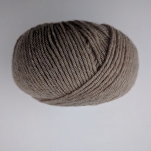 May include: A ball of taupe-colored yarn, tightly wound and textured. The yarn appears to be a neutral shade, suitable for various knitting or crochet projects. The image is a close-up, highlighting the yarn's texture and form.