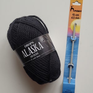 May include: A ball of black Drops Alaska wool yarn with a label that reads "Drops Alaska Uni Colour A wool classic 100% wool" and a gray crochet hook with a blue and orange label that reads "Pony 15 cm 4.5 mm #43410 Made in India"