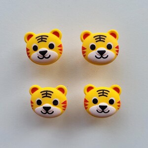 Pode incluir: Quatro botões amarelos com a forma de um rosto de tigre com listras pretas e detalhes vermelhos.