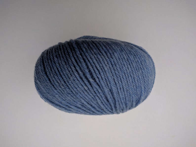 May include: A ball of blue yarn, tightly wound, with visible strands. The yarn has a soft, matte appearance and is suitable for knitting or crocheting projects. The color is a muted, dusty blue.