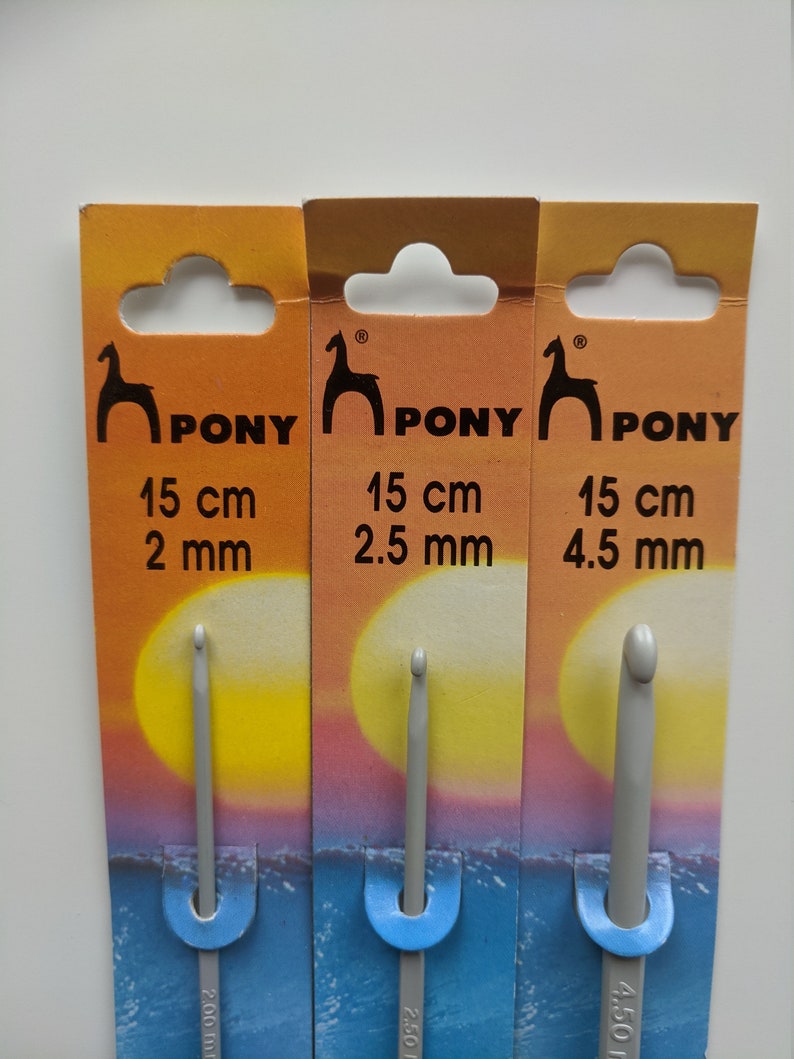 May include: Three Pony brand crochet hooks on their packaging. The hooks are gray and are 15 cm long. The hooks are 2 mm, 2.5 mm, and 4.5 mm in size.