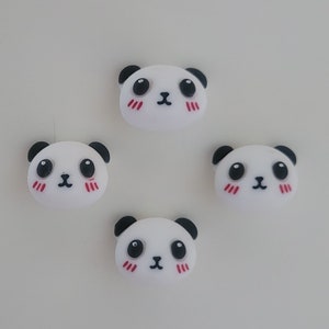Op de afbeelding: Vier witte pandabeergezichtscharms met zwarte ogen, zwarte oren en rode wangen. De charms zijn gemaakt van glad, wit materiaal.