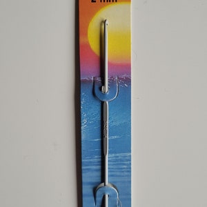 May include: A white Pony brand crochet hook with a 15 cm (6 inch) length and a 2 mm size. The hook is packaged on a blue and orange card with the brand name and size printed on it. The card also has a sunset scene with a yellow sun and blue water.