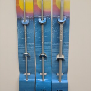 May include: Three gray crochet hooks on individual cards. The cards are blue and white with a sunset and ocean scene. The hooks are labeled with their size in millimeters: 2 mm, 2.5 mm, and 4.5 mm. The cards also include the product number and "Made in India."