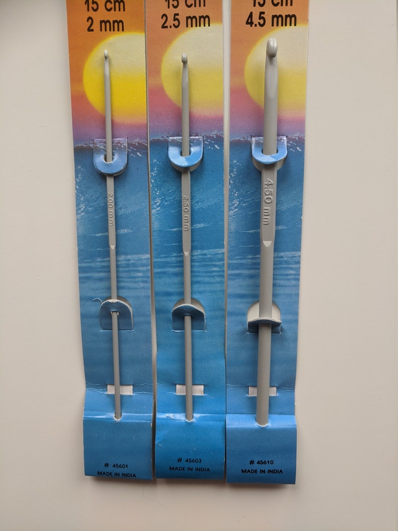 May include: Three gray crochet hooks on individual cards. The cards are blue and white with a sunset and ocean scene. The hooks are labeled with their size in millimeters: 2 mm, 2.5 mm, and 4.5 mm. The cards also include the product number and "Made in India."
