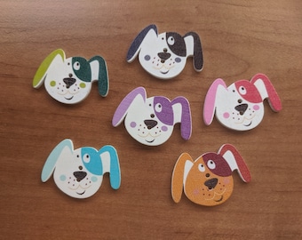 May include: Six wooden dog-shaped buttons with different colored ears and spots. The buttons are white with black eyes and noses, and each has a different colored spot on one ear.
