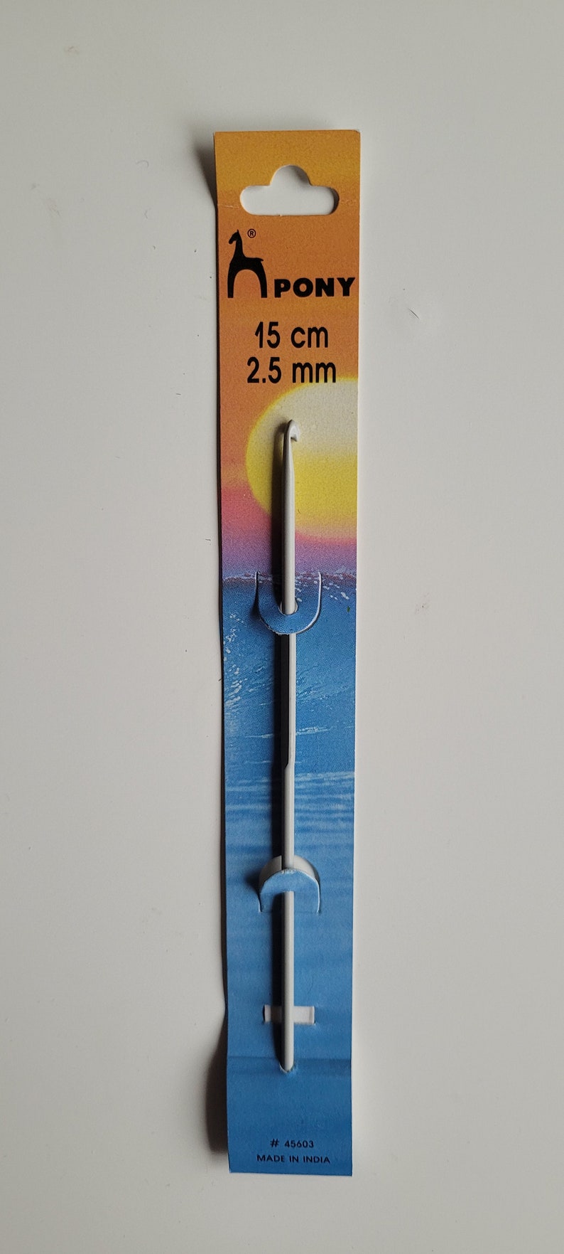 May include: A white Pony brand crochet hook with a 2.5 mm size, packaged on a yellow, orange, and blue card with the text "Pony 15 cm 2.5 mm # 45603 MADE IN INDIA".