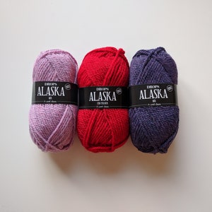May include: Three skeins of yarn in different colors: purple, red, and blue. Each skein has a label that reads "DROPS ALASKA MIX" and a small white circle with a black "G" inside.