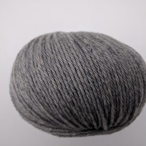 May include: A ball of gray yarn, tightly wound and textured, sits against a plain white background. The yarn appears to be a medium weight, suitable for various knitting or crochet projects. The color is a neutral gray.