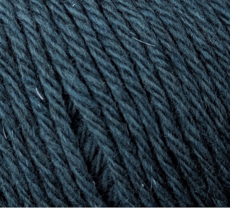 May include: Close-up of dark teal yarn, showing the texture of the fibers. The yarn appears soft and slightly fuzzy, with subtle variations in color. Ideal for knitting or crocheting projects.