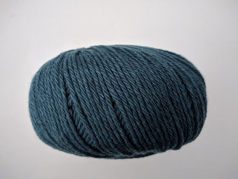 May include: A ball of teal-colored yarn, tightly wound and oval-shaped. The yarn appears to be made of a soft, textured material, ideal for knitting or crocheting projects. The yarn is a solid color with no visible patterns.