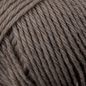 May include: Close-up of a ball of yarn in a neutral, earthy tone. The yarn is tightly wound, showing the texture of the individual strands. The color is a muted brown, suitable for various knitting or crochet projects.