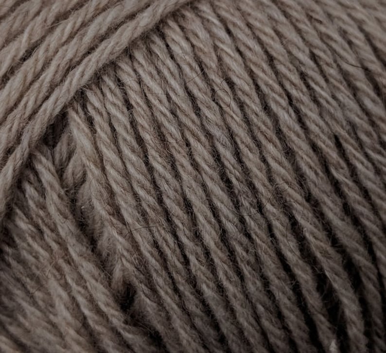 May include: Close-up of a ball of yarn in a neutral, earthy tone. The yarn is tightly wound, showing the texture of the individual strands. The color is a muted brown, suitable for various knitting or crochet projects.