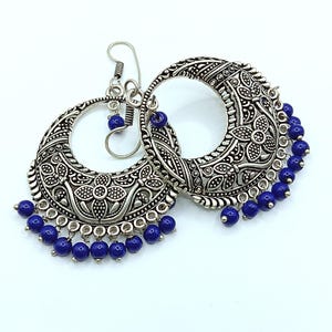May include: Silver hoop earrings with intricate floral designs and dangling blue beads.
