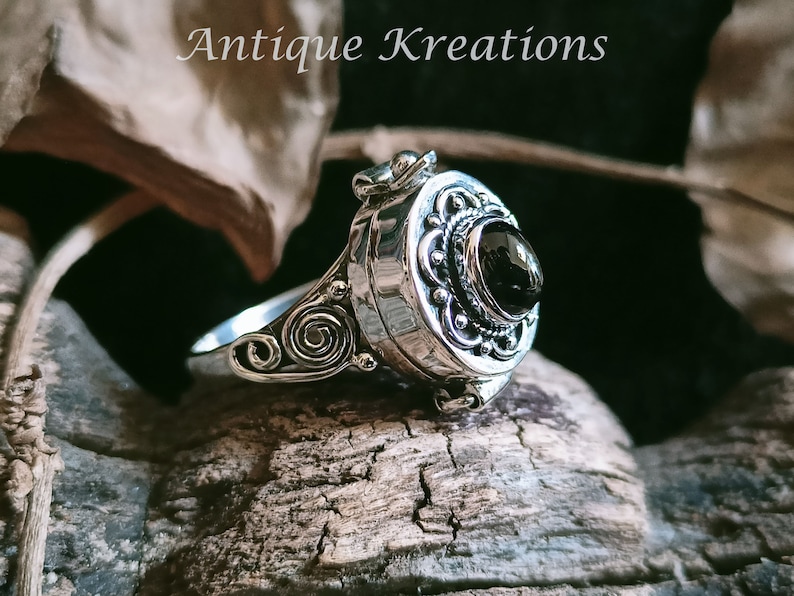 K&ouml;nnte beinhalten: Ein silberner Ring mit einem schwarzen Stein und filigranen Details. Der Ring ist ein Medaillon, das sich &ouml;ffnet und ein kleines Fach enth&uuml;llt.
