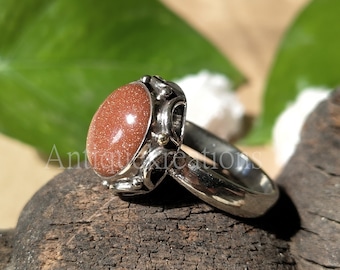 May include: A silver ring with a large, oval-shaped, reddish-brown gemstone. The ring has a detailed, ornate design with small, gold accents.