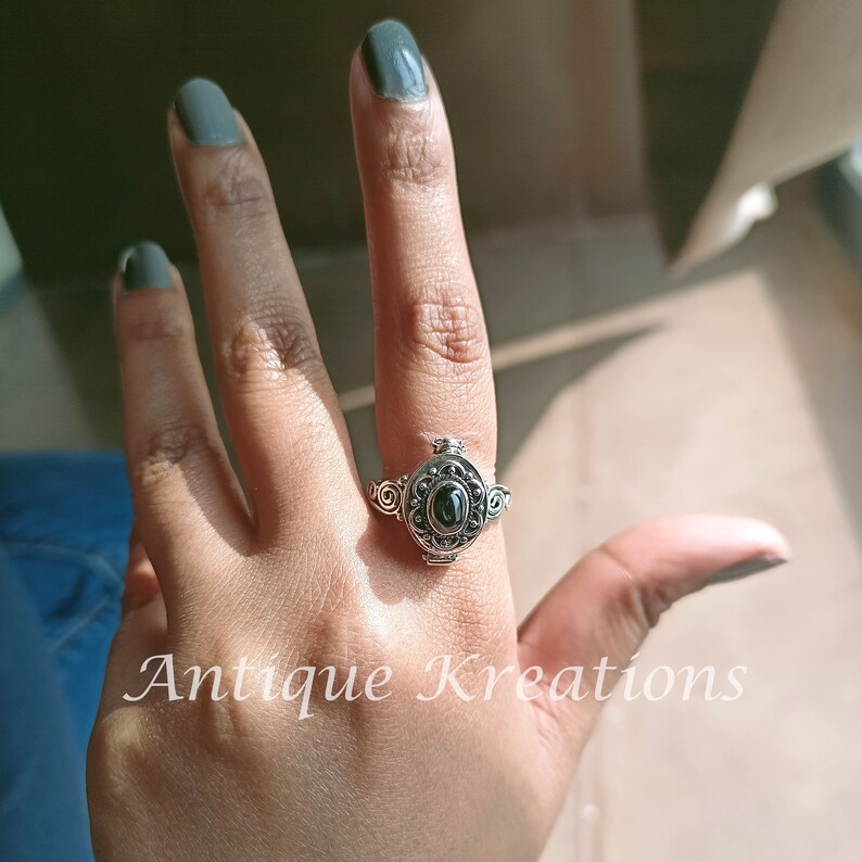 K&ouml;nnte beinhalten: Ein silberner Ring mit einem schwarzen Stein und filigranen Details. Der Ring wird an einem Finger mit dunkelgr&uuml;nem Nagellack getragen.