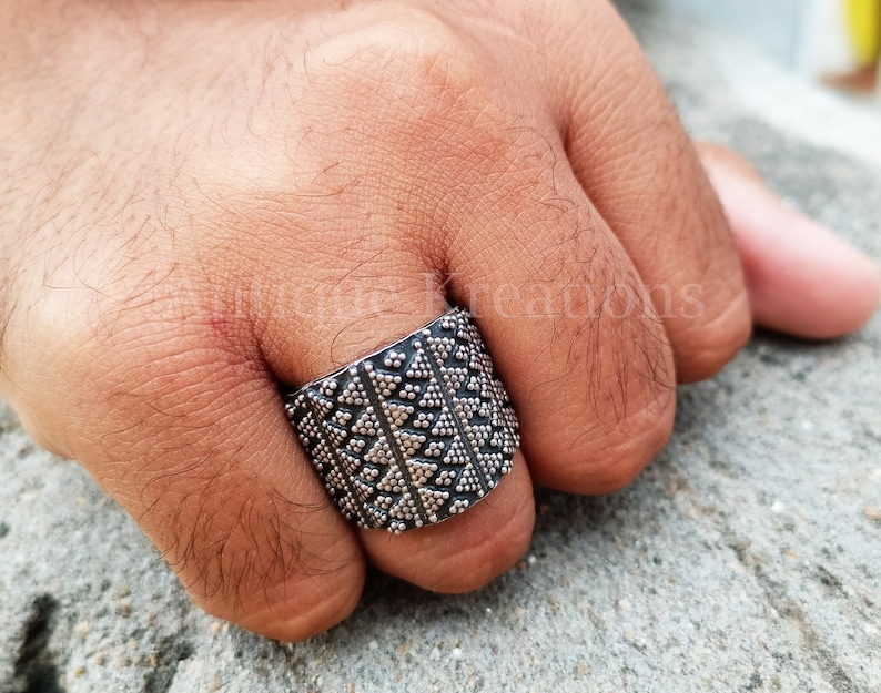 K&ouml;nnte beinhalten: Ein silberner Ring mit geometrischem Muster. Der Ring ist breit und hat eine strukturierte Oberfl&auml;che.