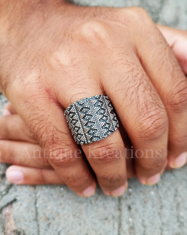 K&ouml;nnte beinhalten: Ein breiter Silberring mit geometrischem Muster. Der Ring ist aus Sterlingsilber gefertigt und hat eine strukturierte Oberfl&auml;che.