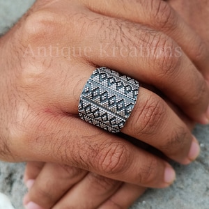 K&ouml;nnte beinhalten: Ein silberner Ring mit geometrischem Muster. Der Ring ist breit und hat eine strukturierte Oberfl&auml;che.