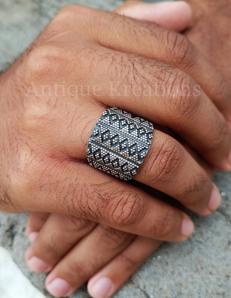 K&ouml;nnte beinhalten: Ein silberner Ring mit geometrischem Muster. Der Ring ist breit und hat eine strukturierte Oberfl&auml;che.