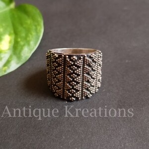 K&ouml;nnte beinhalten: Ein silberner Ring mit einem geometrischen Muster aus kleinen Punkten und Dreiecken. Der Ring ist breit und hat eine strukturierte Oberfl&auml;che.