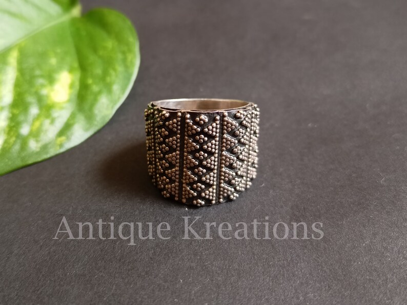 K&ouml;nnte beinhalten: Ein silberner Ring mit einem geometrischen Muster aus kleinen Punkten und Dreiecken. Der Ring ist breit und hat eine strukturierte Oberfl&auml;che.
