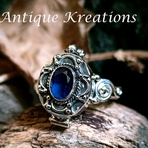 Peut inclure: Une bague en argent avec une pierre précieuse bleue sertie dans un motif de filigrane orné. La bague est ouvrable et possède un couvercle à charnière.