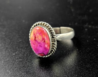 Puede incluir: Un anillo de plata con una piedra ovalada rosa y naranja engastada en un borde de cuerda.