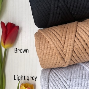 May include: Three spools of thick cotton rope in black, brown, and light grey. The spools are stacked on top of each other.