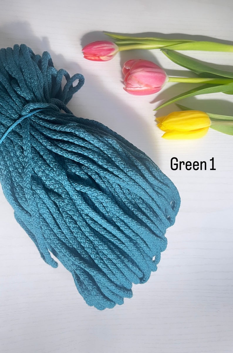 May include: A teal blue cotton rope cord, coiled and ready for crafting projects. The rope is on a white surface with three tulips in the background.