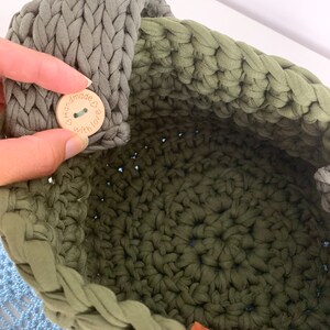 May include: A green crocheted basket with a wooden button that says "Handmade with love" and a brown leather handle.