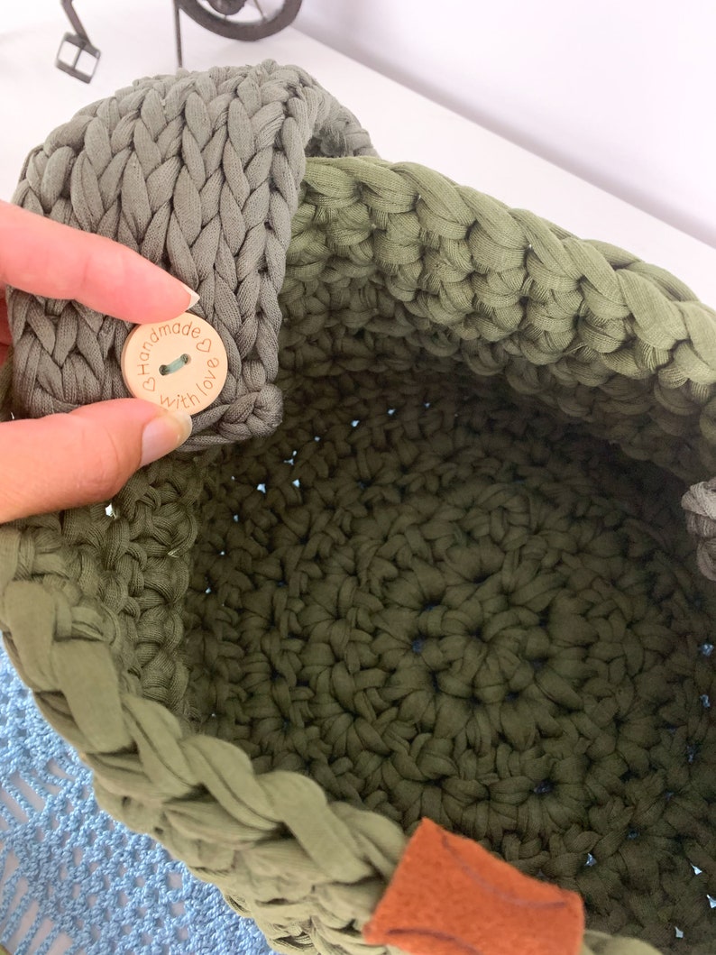 May include: A green crocheted basket with a wooden button that says "Handmade with love" and a brown leather handle.