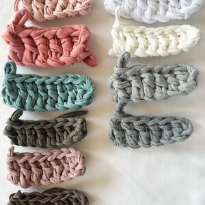 May include: Assortment of 10 crocheted headbands in various colors, including pink, white, gray, brown, and teal. The headbands are made with a chunky yarn and have a simple, textured design.