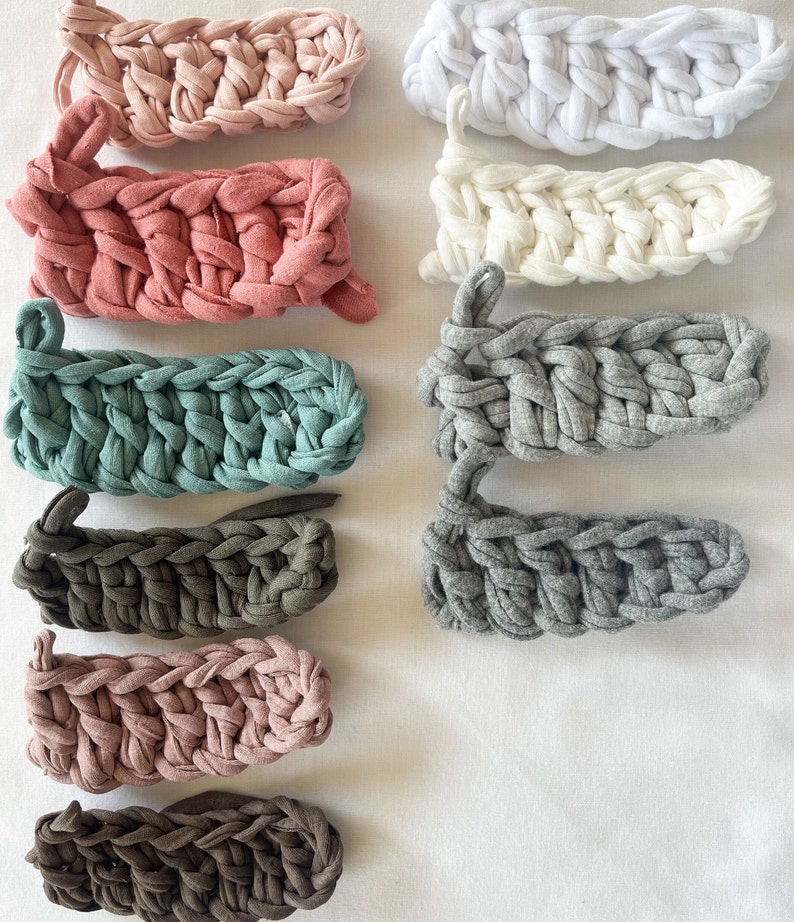 May include: Assortment of 10 crocheted headbands in various colors, including pink, white, gray, brown, and teal. The headbands are made with a chunky yarn and have a simple, textured design.