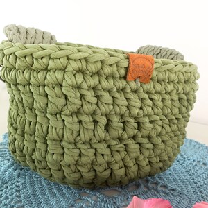 May include: A green crocheted basket with two gray fabric handles and a brown leather tag that says "Handmade with Love".